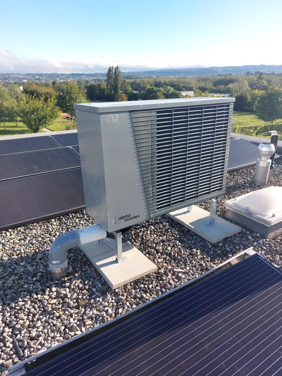 Pompe à chaleur alpha innotec posée sur une toiture terrasse avec panneaux solaires à Denges, Vaud